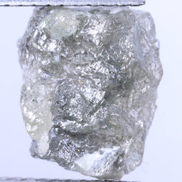 Raw diamond held between tweezers against a light purple background
