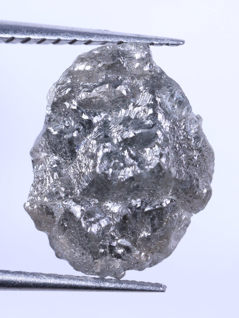 Raw diamond held between tweezers against a light gray background