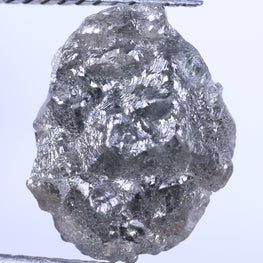 Raw diamond held between tweezers against a light gray background