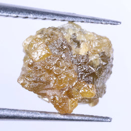 Raw diamond held between tweezers on a white background