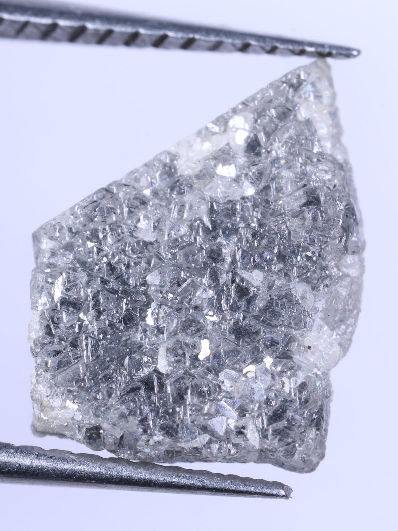 Raw diamond held between tweezers on a light purple background