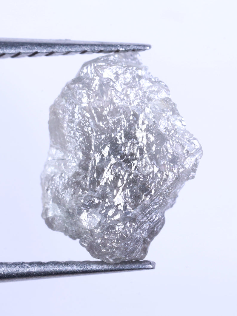 Raw diamond held between tweezers on a light gray background