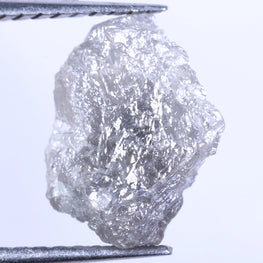 Raw diamond held between tweezers on a light gray background
