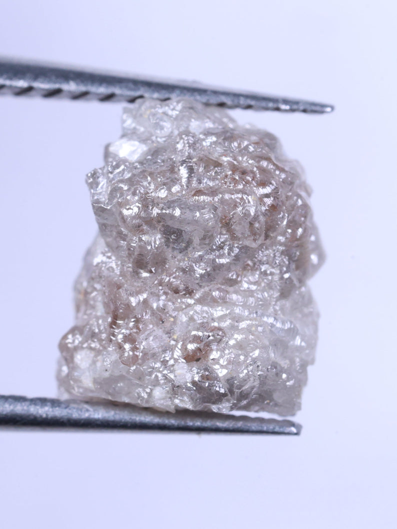 Raw diamond held between tweezers against a light purple background