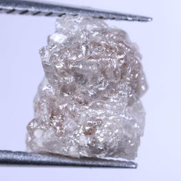 Raw diamond held between tweezers against a light purple background