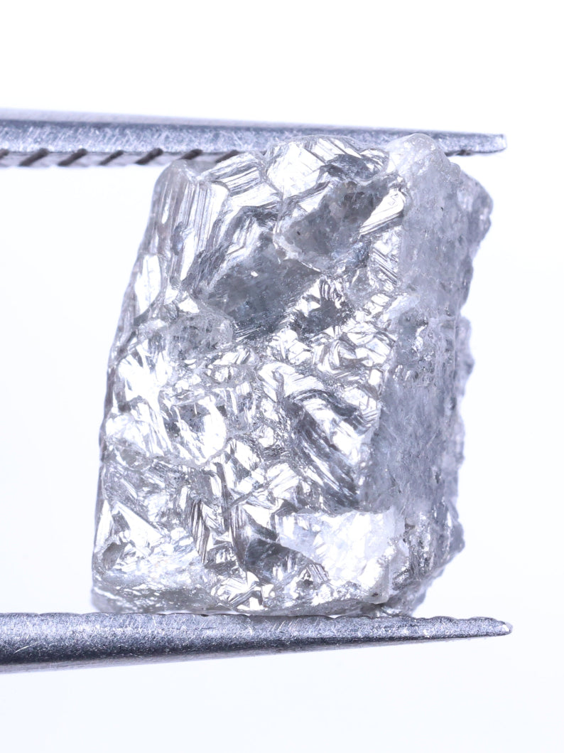 Raw diamond held by tweezers on a white background