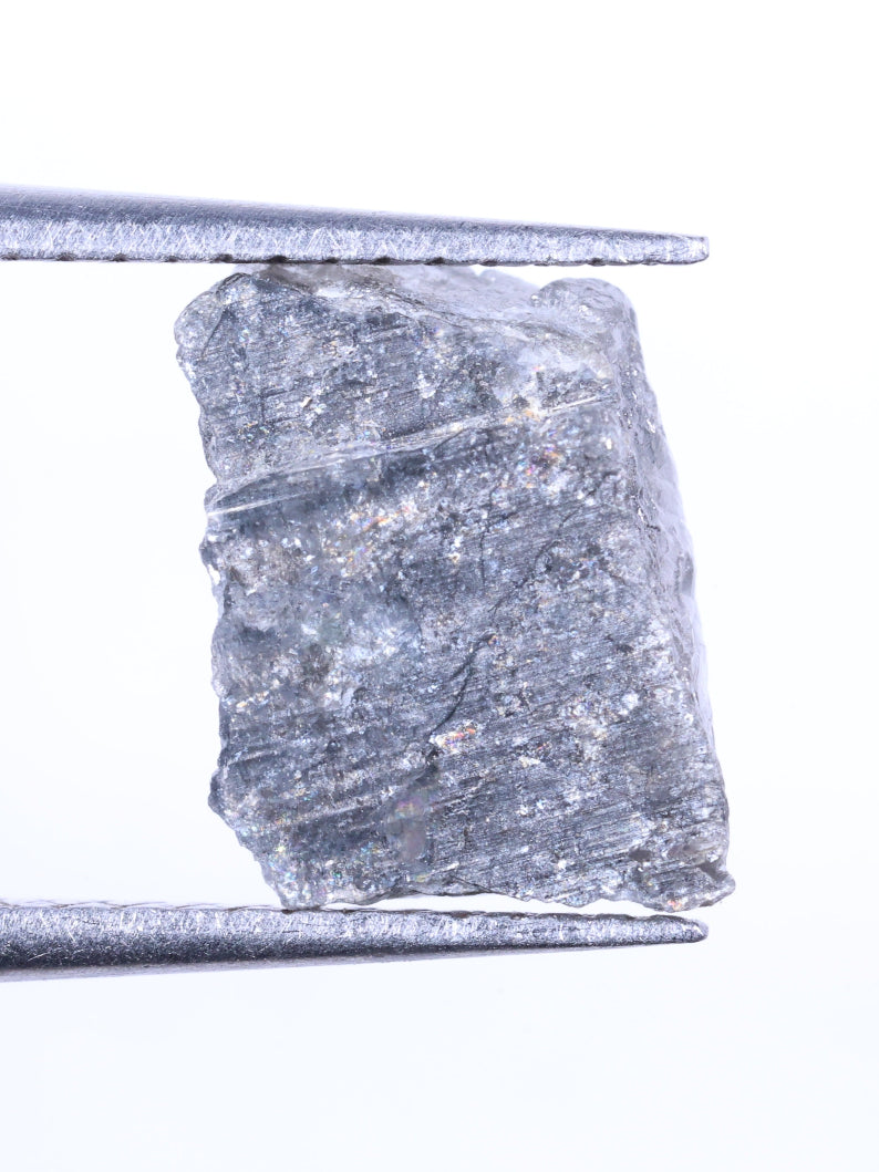 Raw diamond held between tweezers on a white background