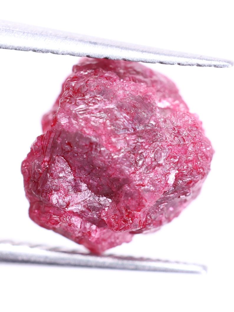 Raw pink diamond held between tweezers on a white background