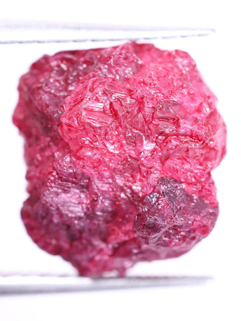 pink rough diamond held by tweezers against a white background