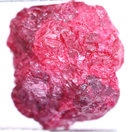 pink rough diamond held by tweezers against a white background