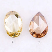 Two lab grown diamonds displayed on white background, including a fancy light yellow oval cut diamond labeled 1 and a champagne pear shaped diamond labeled 2, sustainably created loose stones for engagement rings.