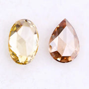 Two lab grown diamonds displayed on white background, including a fancy light yellow oval cut diamond labeled 1 and a champagne pear shaped diamond labeled 2, sustainably created loose stones for engagement rings.