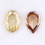 Two lab grown diamonds displayed on white background, including a fancy light yellow oval cut diamond labeled 1 and a champagne pear shaped diamond labeled 2, sustainably created loose stones for engagement rings.