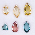 Six lab grown colored diamonds displayed on white background featuring pear, marquise and oval cuts in fancy yellow, champagne, blue and pink shades, ideal for custom engagement rings and fine jewelry settings.