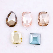 Five lab grown diamonds in various shapes including pear, cushion, and square step cut, displayed in pastel shades of pink, champagne, yellow, and blue on a white background.