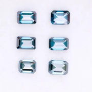 Six emerald cut lab grown blue diamonds in teal and deep ocean blue tones arranged on a white background, showcasing step cut facets and rectangular shapes for fine jewelry and engagement ring settings.
