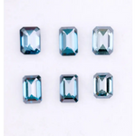 Six emerald cut lab grown blue diamonds in teal and deep ocean blue tones arranged on a white background, showcasing step cut facets and rectangular shapes for fine jewelry and engagement ring settings.