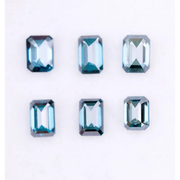 Six emerald cut lab grown blue diamonds in teal and deep ocean blue tones arranged on a white background, showcasing step cut facets and rectangular shapes for fine jewelry and engagement ring settings.
