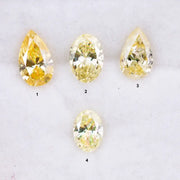 Four fancy yellow lab grown diamonds in pear and oval brilliant cuts displayed on white background, showcasing vivid yellow color, high clarity, and precision faceting.