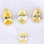 Four fancy yellow lab grown diamonds in pear and oval brilliant cuts displayed on white background, showcasing vivid yellow color, high clarity, and precision faceting.