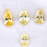 Four fancy yellow lab grown diamonds in pear and oval brilliant cuts displayed on white background, showcasing vivid yellow color, high clarity, and precision faceting.
