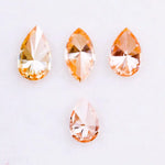 Four fancy colored lab grown diamonds in pear and marquise cuts, featuring vibrant orange and soft peach tones, displayed on a white background as loose sustainable gemstones.