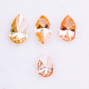 Four fancy colored lab grown diamonds in pear and marquise cuts, featuring vibrant orange and soft peach tones, displayed on a white background as loose sustainable gemstones.