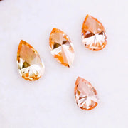 Four fancy colored lab grown diamonds in pear and marquise cuts, featuring vibrant orange and soft peach tones, displayed on a white background as loose sustainable gemstones.