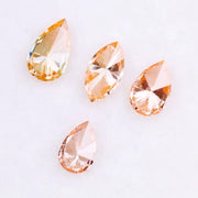 Four fancy colored lab grown diamonds in pear and marquise cuts, featuring vibrant orange and soft peach tones, displayed on a white background as loose sustainable gemstones.