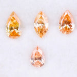 Four fancy colored lab grown diamonds in pear and marquise cuts, featuring vibrant orange and soft peach tones, displayed on a white background as loose sustainable gemstones.