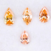 Four fancy colored lab grown diamonds in pear and marquise cuts, featuring vibrant orange and soft peach tones, displayed on a white background as loose sustainable gemstones.