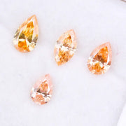 Four fancy colored lab grown diamonds in pear and marquise cuts, featuring vibrant orange and soft peach tones, displayed on a white background as loose sustainable gemstones.