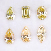Six fancy yellow lab grown diamonds in pear, emerald, oval, and marquise cuts displayed on a white background, showcasing brilliant sparkle and canary color tones.