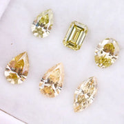 Six fancy yellow lab grown diamonds in pear, emerald, oval, and marquise cuts displayed on a white background, showcasing brilliant sparkle and canary color tones.