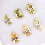 Six fancy yellow lab grown diamonds in pear, emerald, oval, and marquise cuts displayed on a white background, showcasing brilliant sparkle and canary color tones.