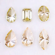 Six fancy yellow lab grown diamonds in pear, emerald, oval, and marquise cuts displayed on a white background, showcasing brilliant sparkle and canary color tones.