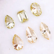 Six fancy yellow lab grown diamonds in pear, emerald, oval, and marquise cuts displayed on a white background, showcasing brilliant sparkle and canary color tones.