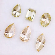 Six fancy yellow lab grown diamonds in pear, emerald, oval, and marquise cuts displayed on a white background, showcasing brilliant sparkle and canary color tones.