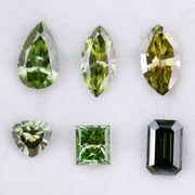 Six fancy color lab grown diamonds in green and yellow shades displayed on white background, featuring pear, marquise, heart, princess, and emerald cuts.