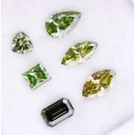 Six fancy color lab grown diamonds in green and yellow shades displayed on white background, featuring pear, marquise, heart, princess, and emerald cuts.