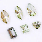 Six fancy color lab grown diamonds in green and yellow shades displayed on white background, featuring pear, marquise, heart, princess, and emerald cuts.