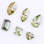 Six fancy color lab grown diamonds in green and yellow shades displayed on white background, featuring pear, marquise, heart, princess, and emerald cuts.