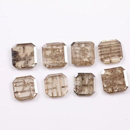 Eight emerald cut lab grown diamonds in champagne tones featuring visible natural-style inclusions and geometric internal patterns, arranged on a white background for fine jewelry selection.