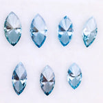 Seven marquise cut blue lab grown diamonds in vivid teal and aqua shades displayed on a white background, showcasing brilliant faceting and elongated shapes for engagement rings or custom jewelry.