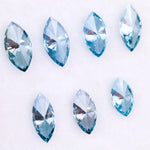 Seven marquise cut blue lab grown diamonds in vivid teal and aqua shades displayed on a white background, showcasing brilliant faceting and elongated shapes for engagement rings or custom jewelry.