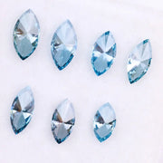 Seven marquise cut blue lab grown diamonds in vivid teal and aqua shades displayed on a white background, showcasing brilliant faceting and elongated shapes for engagement rings or custom jewelry.