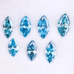 Seven marquise cut blue lab grown diamonds in vivid teal and aqua shades displayed on a white background, showcasing brilliant faceting and elongated shapes for engagement rings or custom jewelry.