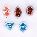 Five loose lab grown diamonds displayed on a white background, featuring three pink diamonds in oval, pear, and round cuts, alongside two vivid blue diamonds in heart and oval shapes, showcasing brilliant faceting and high clarity.