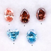 Five loose lab grown diamonds displayed on a white background, featuring three pink diamonds in oval, pear, and round cuts, alongside two vivid blue diamonds in heart and oval shapes, showcasing brilliant faceting and high clarity.