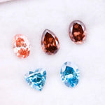 Five loose lab grown diamonds displayed on a white background, featuring three pink diamonds in oval, pear, and round cuts, alongside two vivid blue diamonds in heart and oval shapes, showcasing brilliant faceting and high clarity.